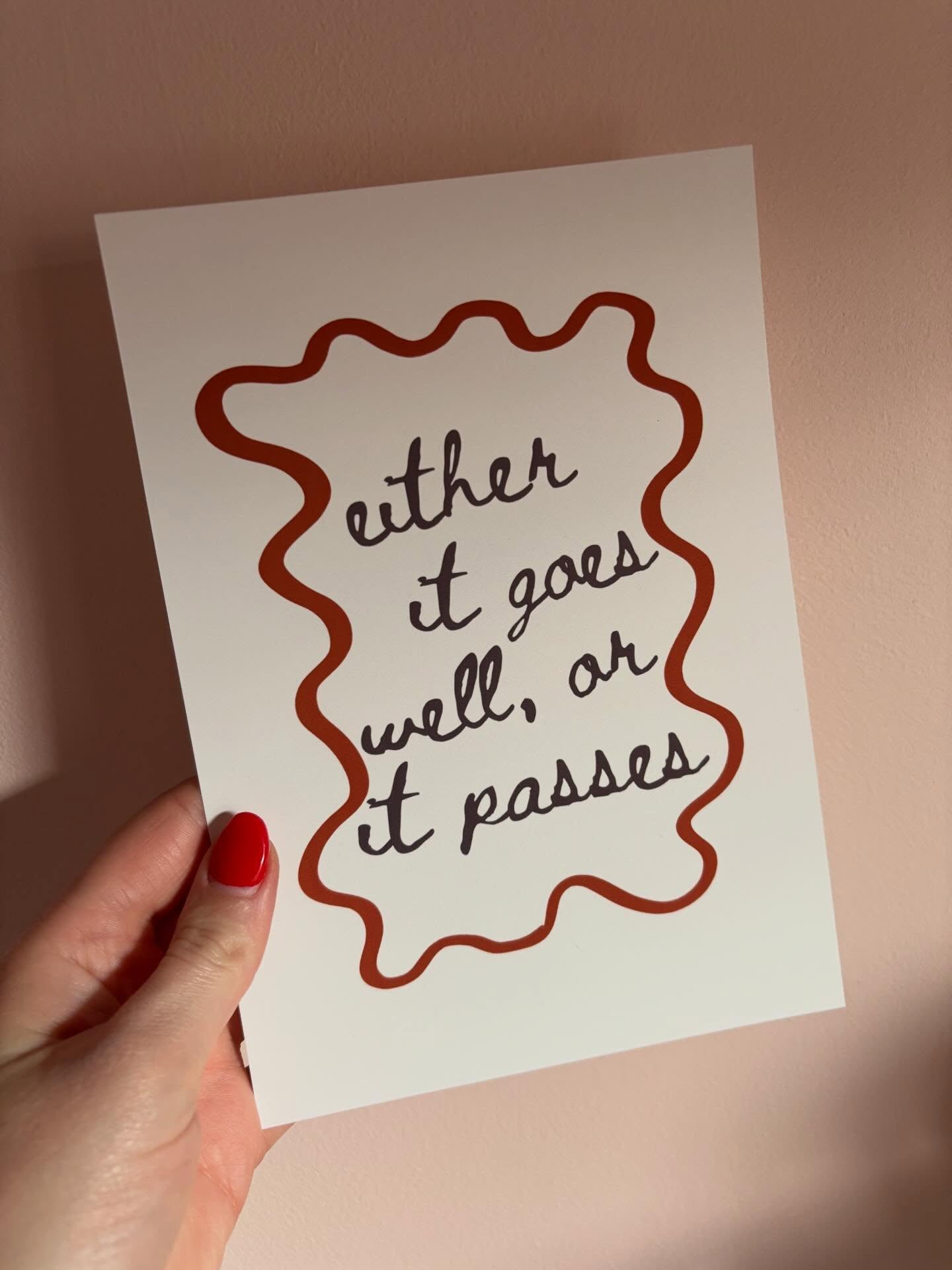 Cream 'either it goes well, or it passes' print with a wavy red border held against a pink wall