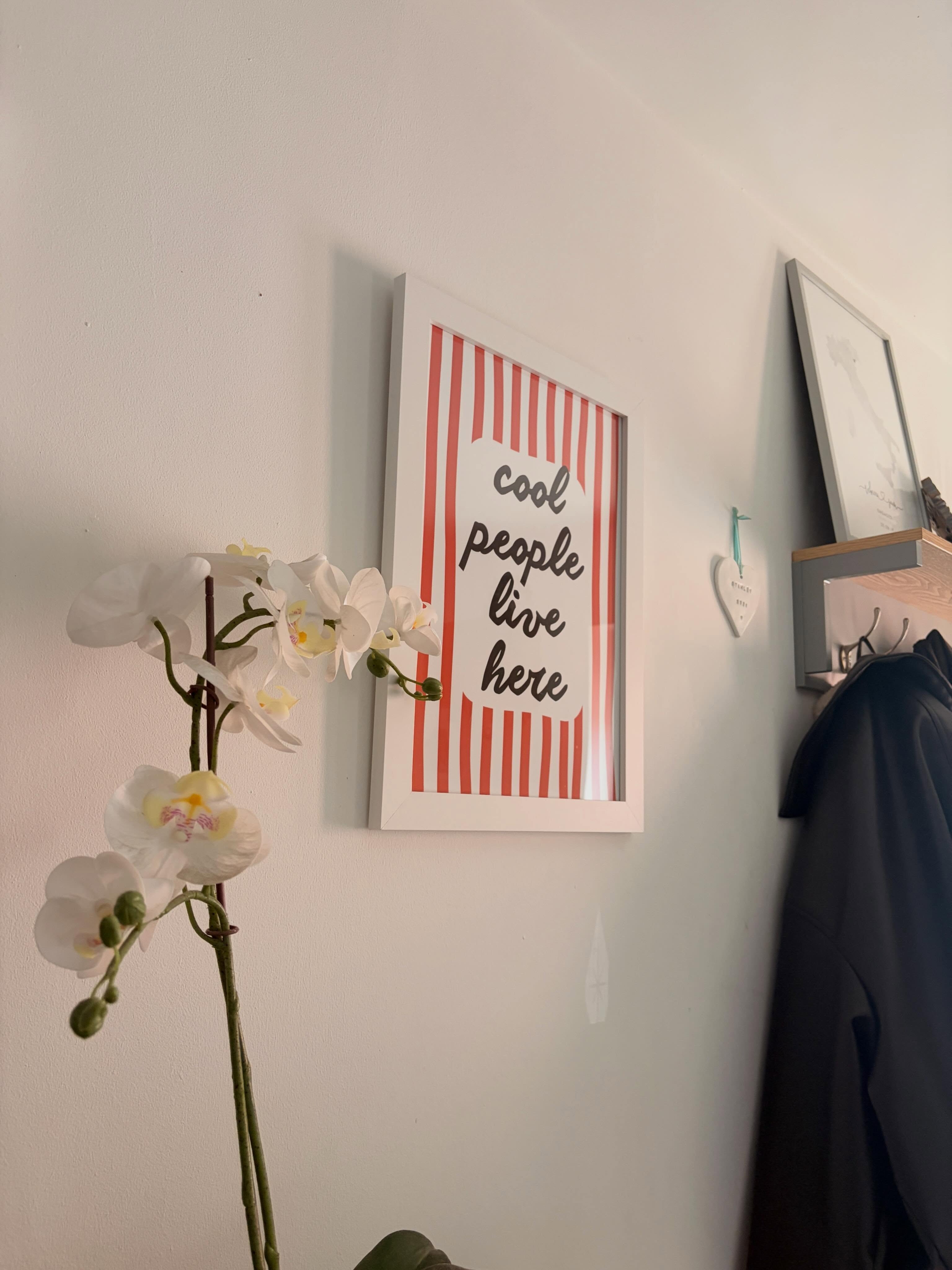 Framed 'cool people live here' print with red stripes hanging in a hallway beside an orchid