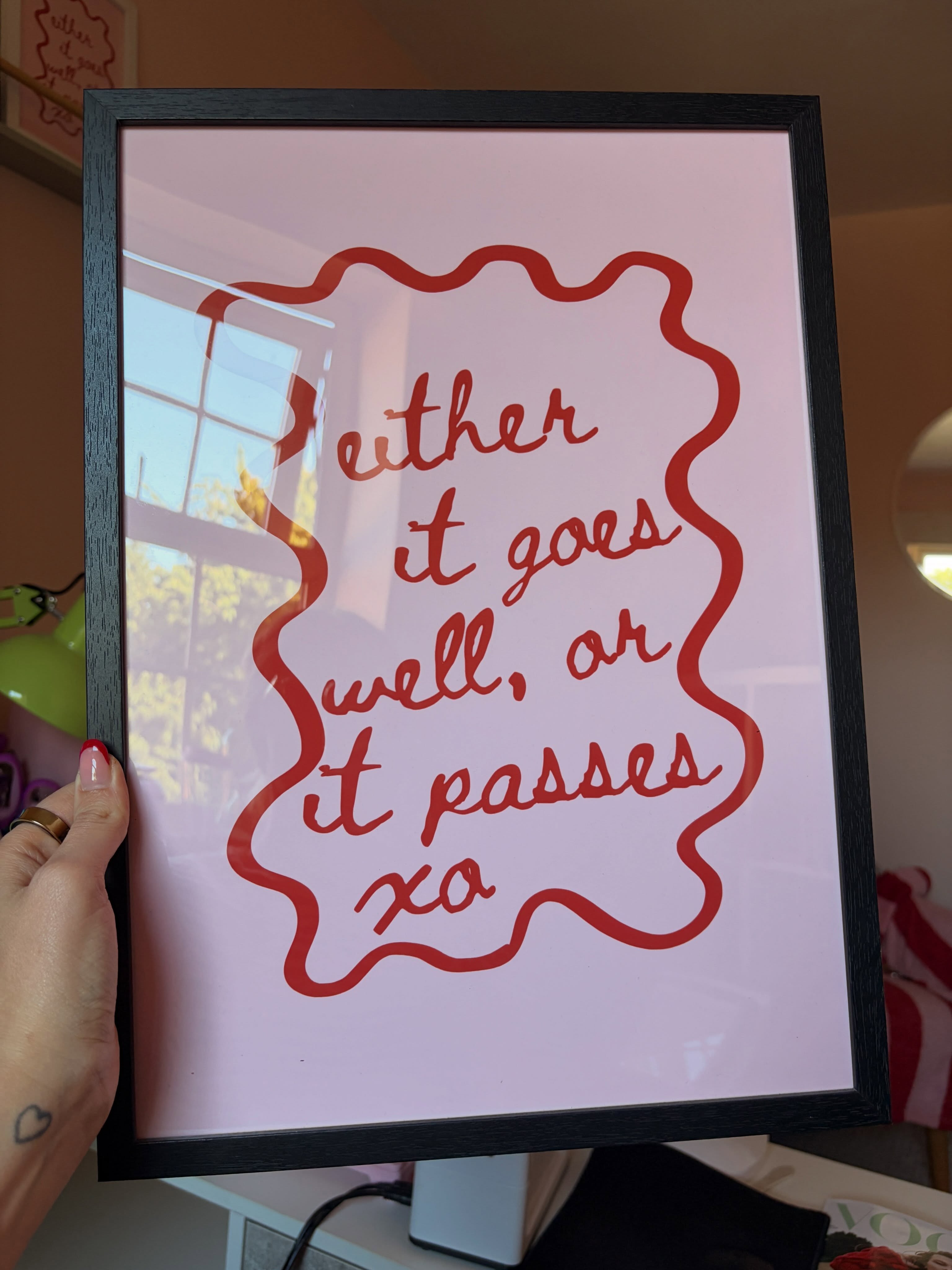 Pink framed print reading 'either it goes well, or it passes' in red script